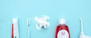 Close up of a toothbrush, toothpaste, irrigator, mouthwash for teeth, dental mirror with white molar tooth model and Protective vortex around tooth on blurred blue background. Oral Care Concept. Concept of oral hygiene in the family