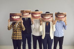 Diverse group of people holding up pictures of smiles that cover their faces illustrating that Grand Avenue Smiles has a team dedicated to bringing you the best dental care available.